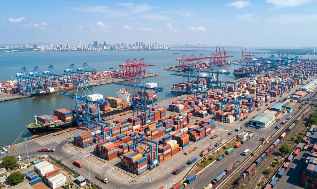 Aerial view of a busy port terminal with cranes, container stacks and city skyline